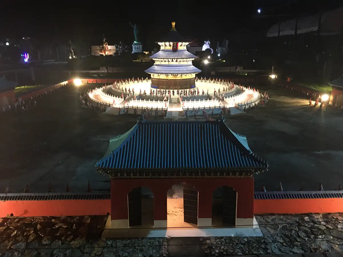 a nighttime photo of a brightly lit, multi-tiered traditional chinese-style temple surrounded by a circular plaza with…