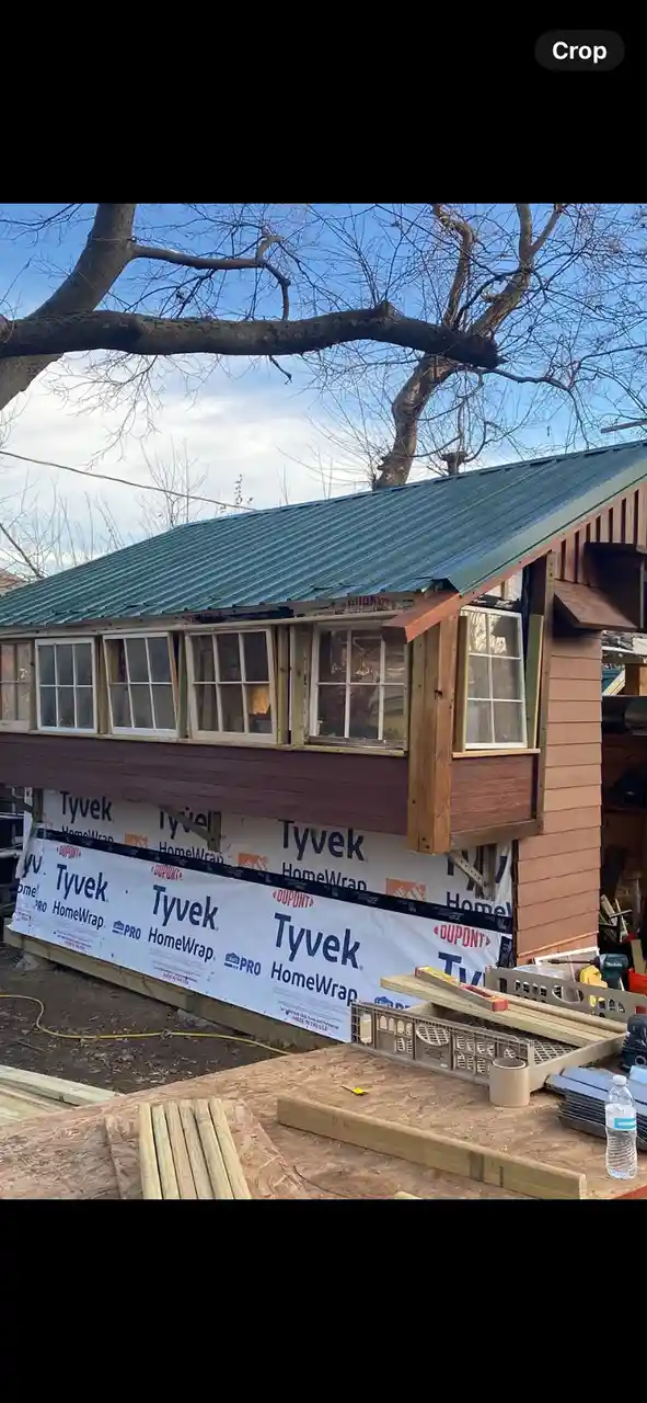 An image of a house under construction with a green metal roof, bare trees in the background, and Tyvek HomeWrap covering…