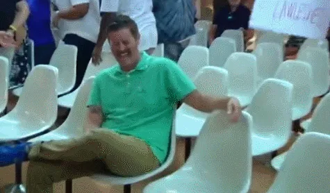 A man in a green polo shirt sits in a row of white plastic chairs, visibly laughing uncontrollably in a sequence of frames…
