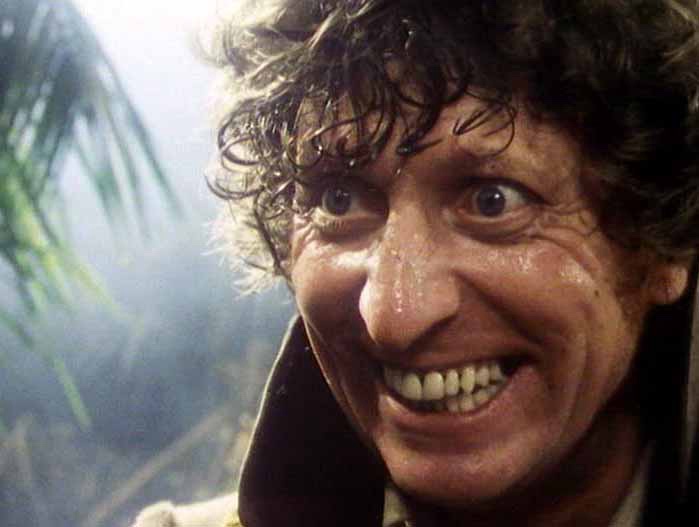 A close-up of a man with wild, wet-looking curly hair and a wide, toothy grin, his eyes wide open and looking slightly…