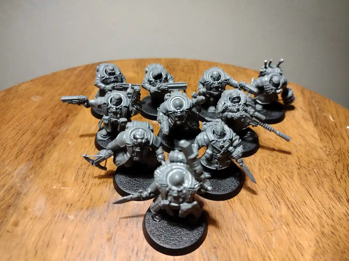 A group of unpainted, gray miniature sci-fi soldiers in detailed armor and holding various weapons are arranged on a wooden…