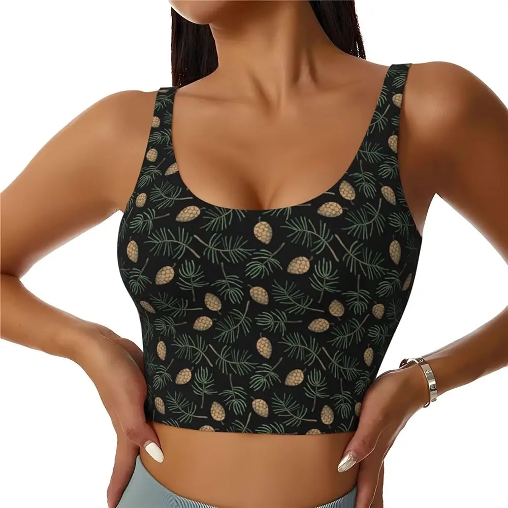 A woman wearing a black crop top with a repeating pattern of pinecones and pine needles, hands on hips, showcasing the…