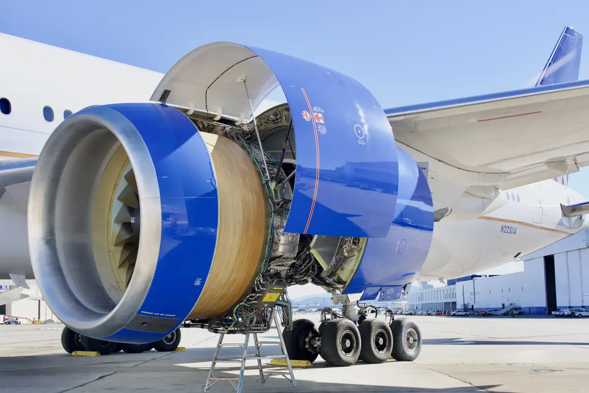 A close-up photo of a large commercial airplane engine with its cowling open, revealing internal components during…
