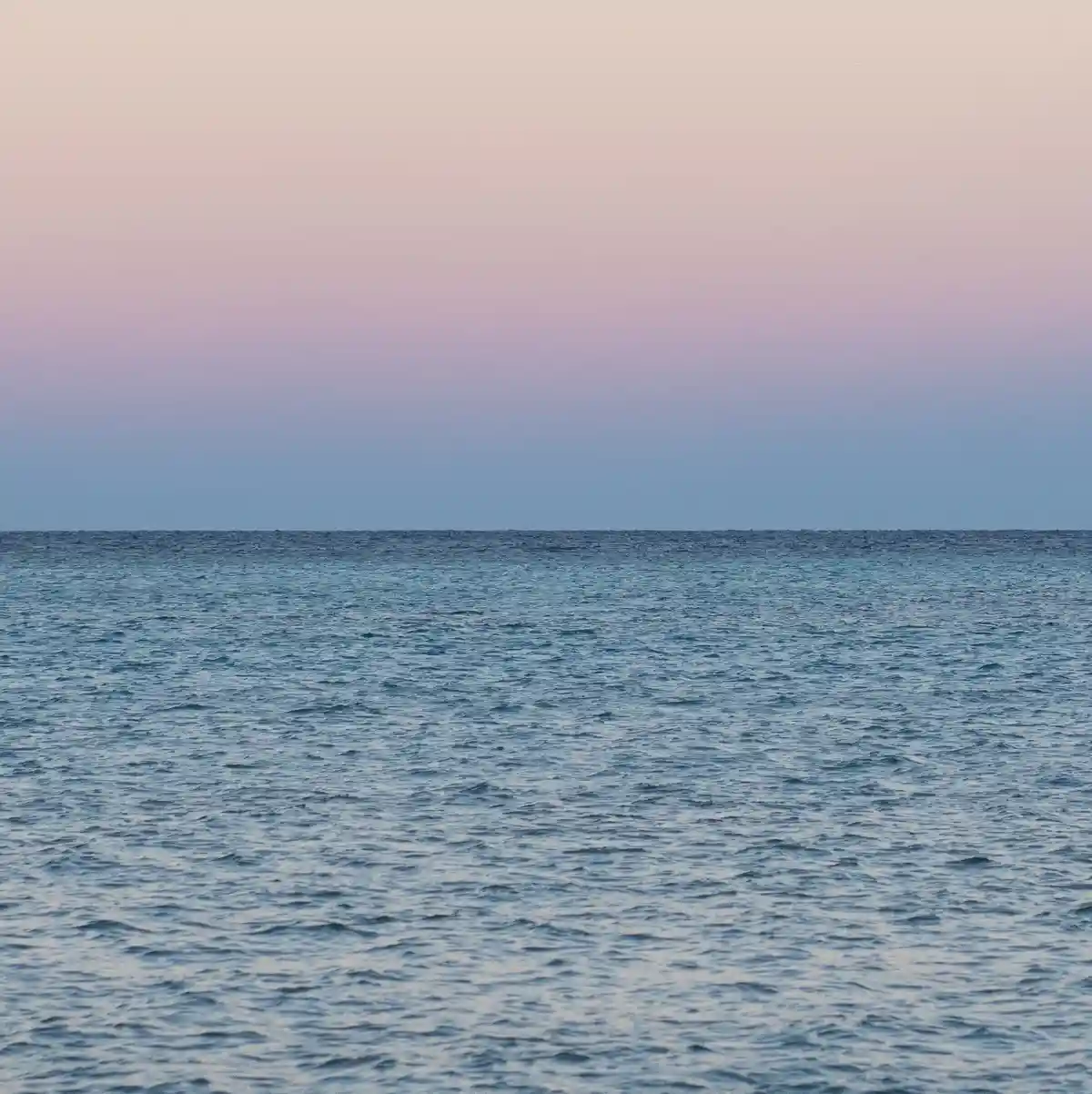 A serene photograph of a calm ocean at dusk, with a gradient sky transitioning from soft pink to blue above the horizon. The…
