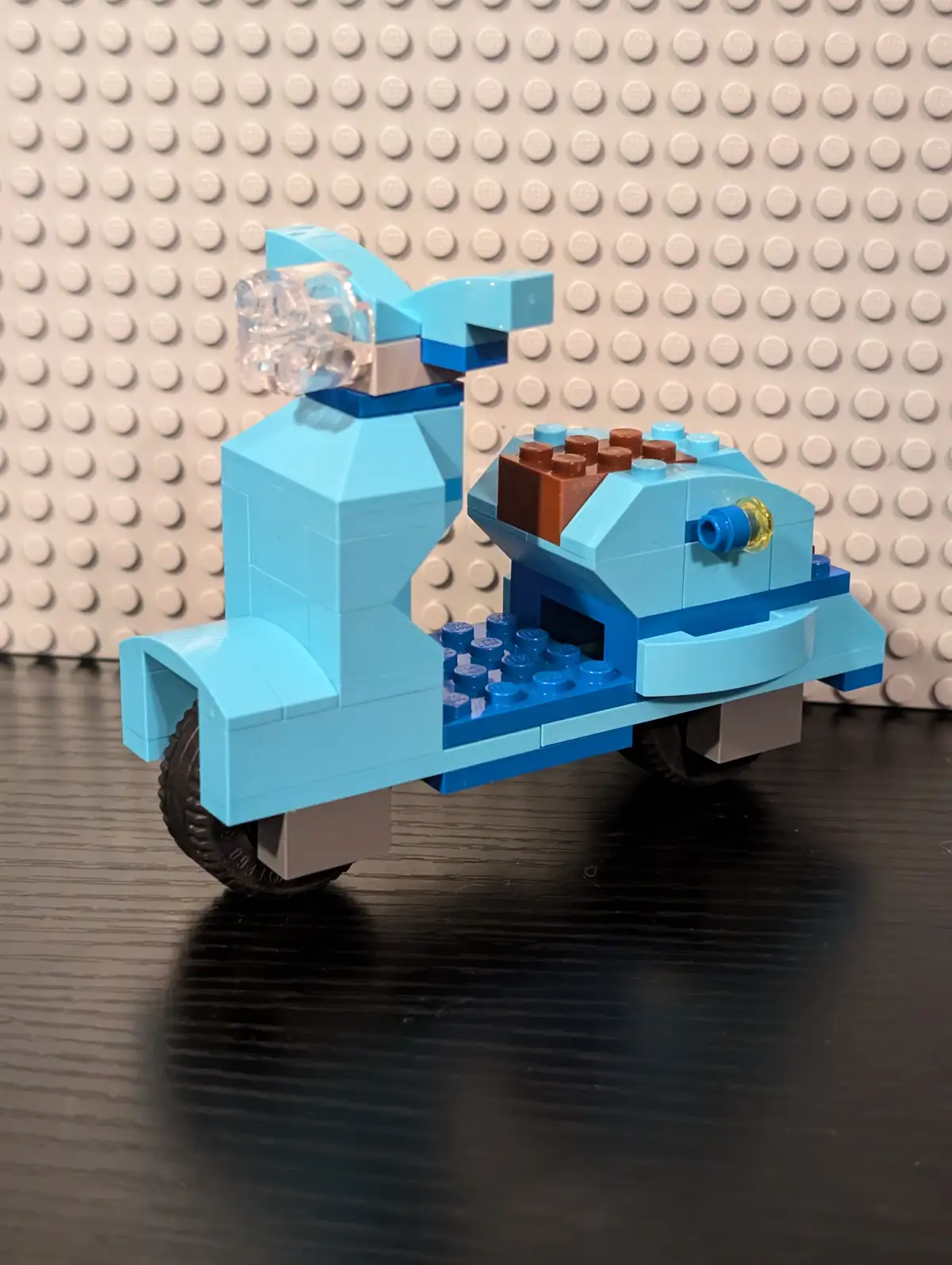 A handmade LEGO scooter model, primarily light blue with dark blue accents and black wheels, is displayed on a dark wooden…