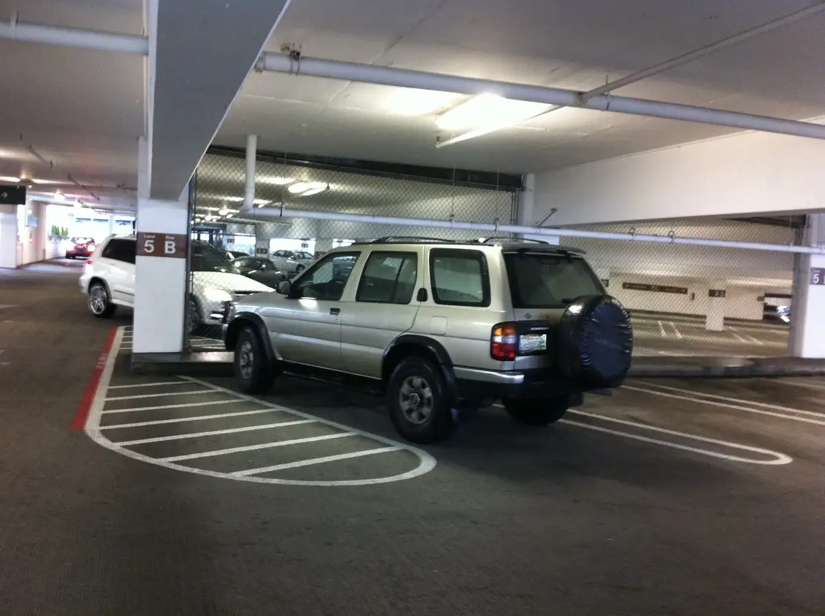 A silver SUV is parked diagonally in a handicapped parking space marked with white lines and a red curb in an indoor parking…
