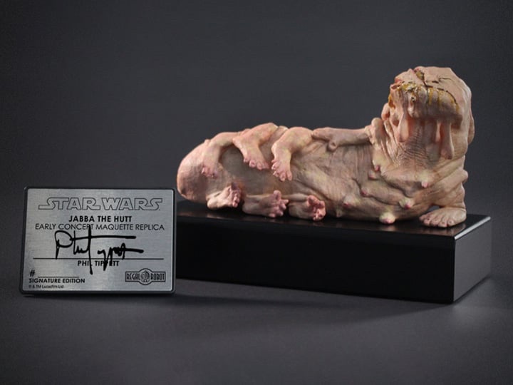 A detailed, flesh-toned maquette replica of Jabba the Hutt lies on a black display stand, next to a silver plaque that reads…