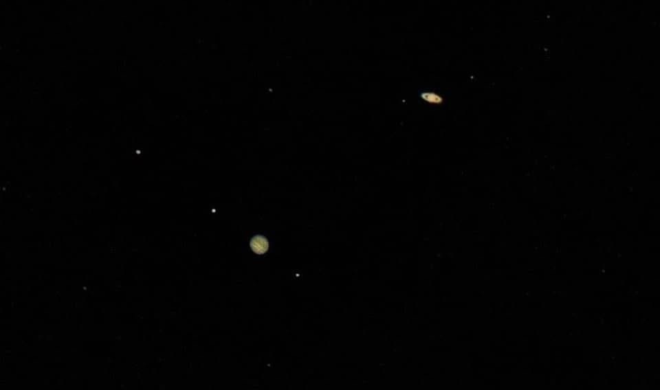 A dark space image showing a few distant celestial bodies, including a prominent yellowish planet with bands and a smaller…