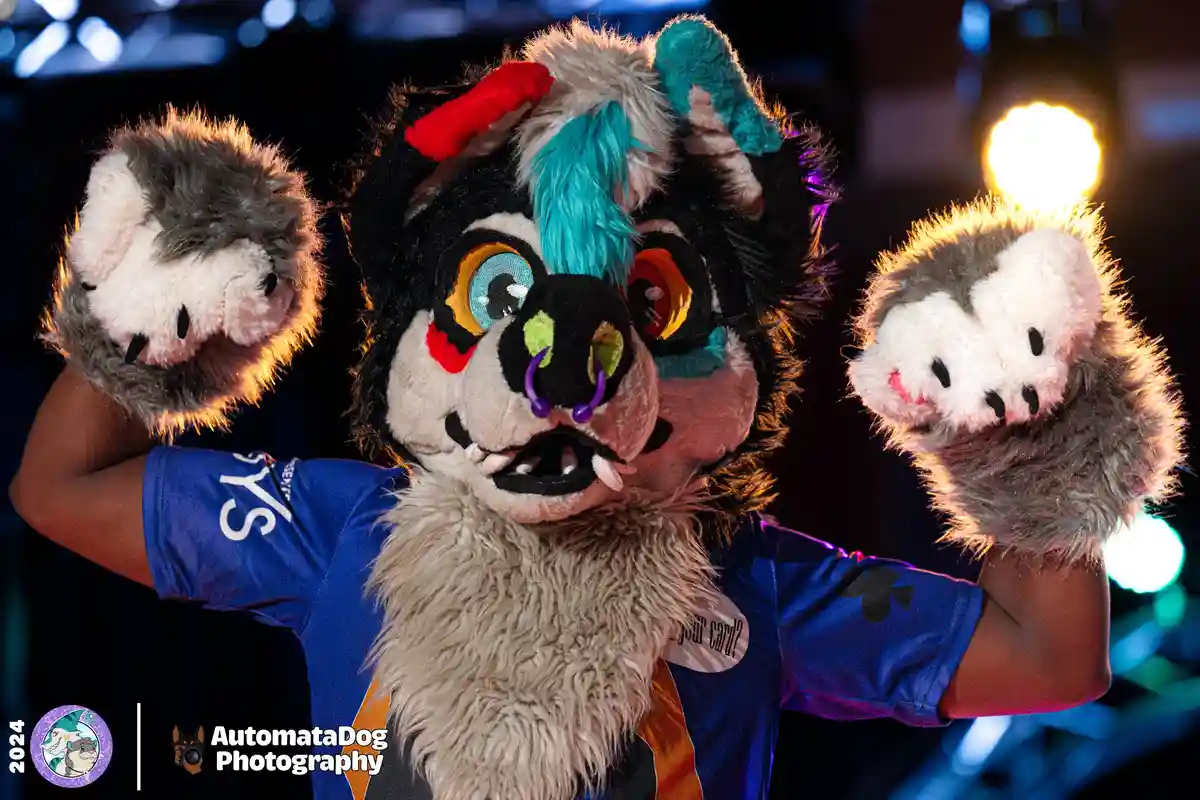 A person in a colorful, detailed fursuit resembling a stylized canine with turquoise and red hair, large eyes, and purple…