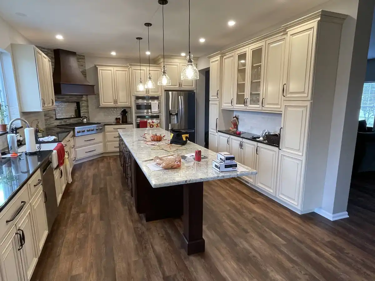 A spacious, modern kitchen with white cabinets, dark wood flooring, and a large central island. The island has a granite…