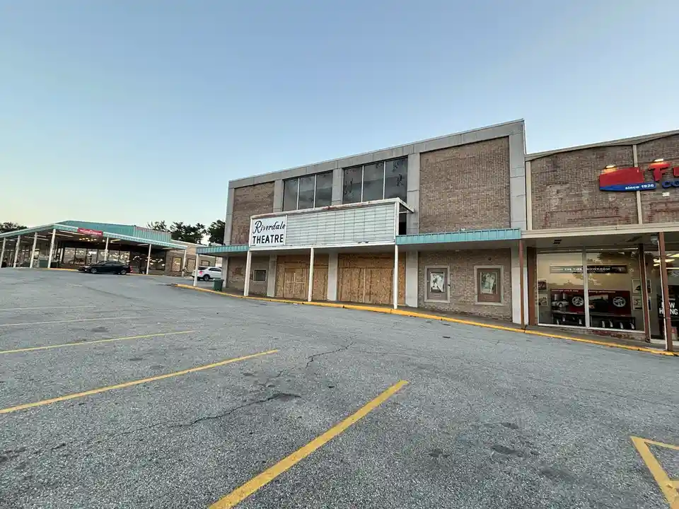 An exterior photo of the Riverdale Theatre, a brick building with boarded-up windows and doors, showing signs of disuse or…