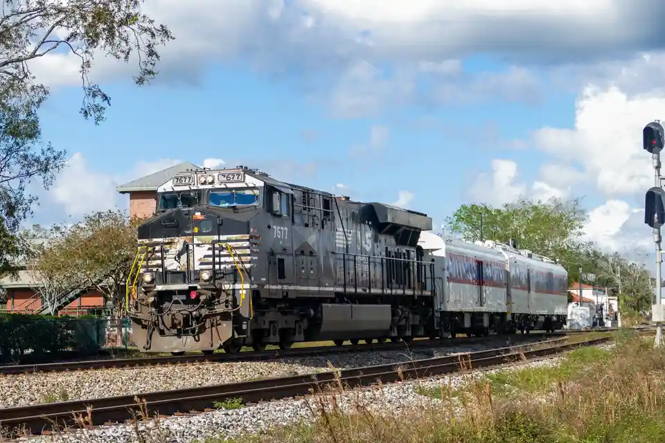 A weathered, gray diesel locomotive numbered 7677, part of the Florida Southern Railroad, is shown on tracks with a…