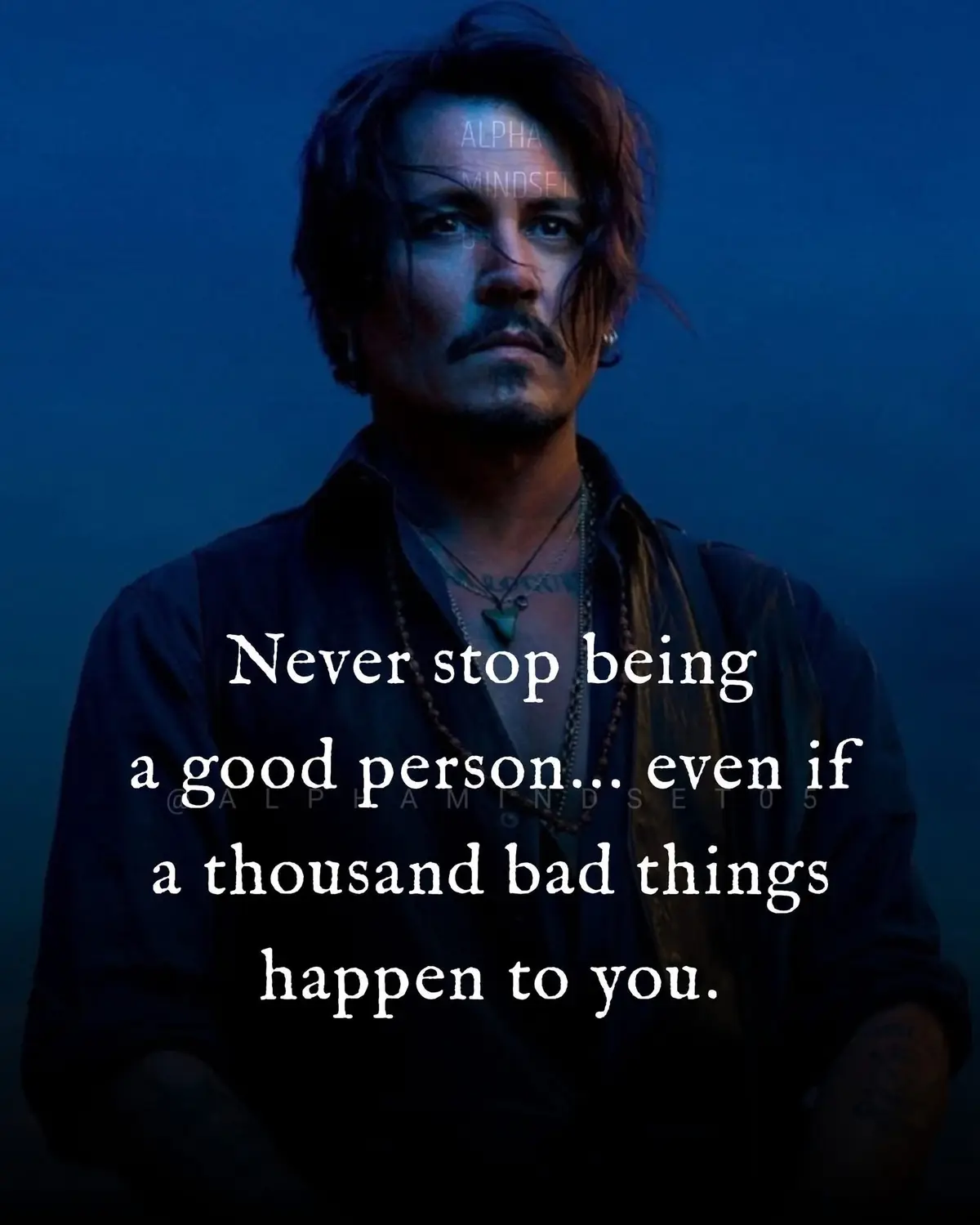 A man with dark hair, a mustache, and multiple necklaces stares intently at the viewer against a dark blue background…