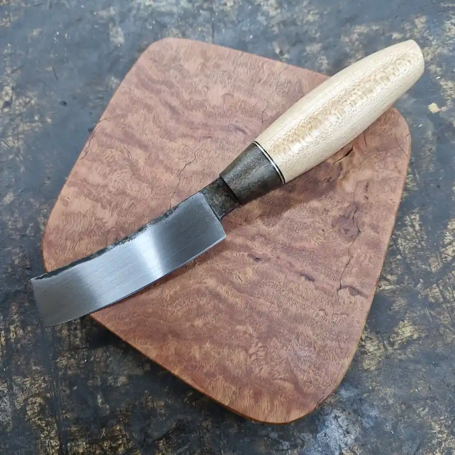 A close-up photo shows a handcrafted woodworking chisel with a light-colored wooden handle and a polished metal blade…