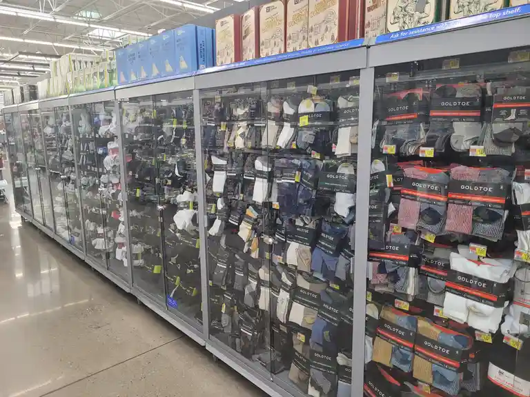 A long aisle in a retail store filled with glass-fronted display cases packed with GoldToe brand socks. The top shelf holds…