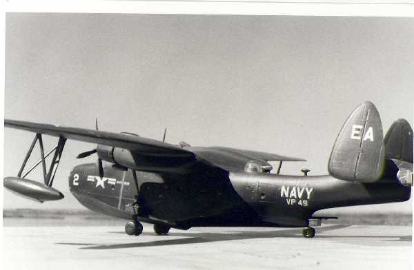 A black-and-white photo of a vintage U.S. Navy flying boat on a runway, with 'NAVY VP 49' and 'EA' visible on its tail and…
