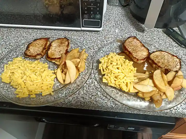 Two identical plates of food sit side-by-side on a kitchen counter, each containing two grilled pork chops, macaroni and…