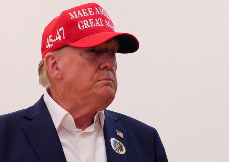 A man wearing a red cap with the text 'MAKE AMERICA GREAT AGAIN' and '45-47' on it, looking off to the side with a serious…