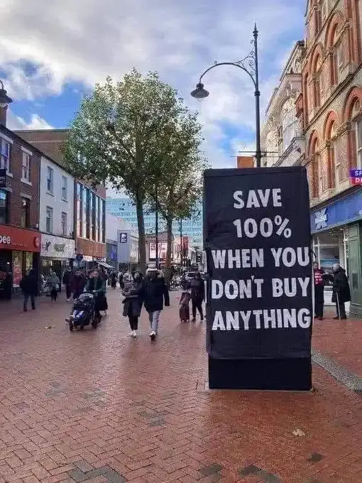 A black banner stands on a brick pedestrian street, displaying white text that reads 'SAVE 100% WHEN YOU DON'T BUY…