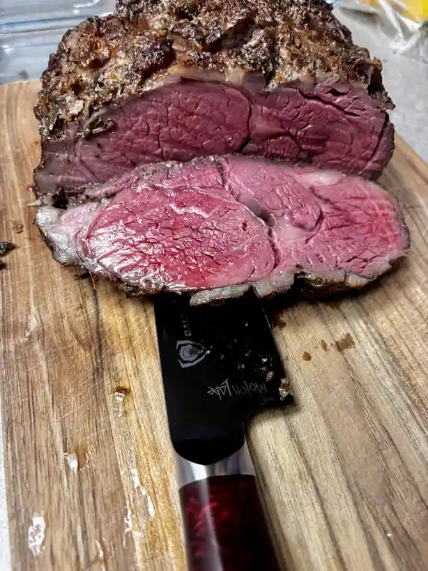 A close-up photo shows a large, sliced roast beef on a wooden cutting board, with a black-handled knife resting in front…