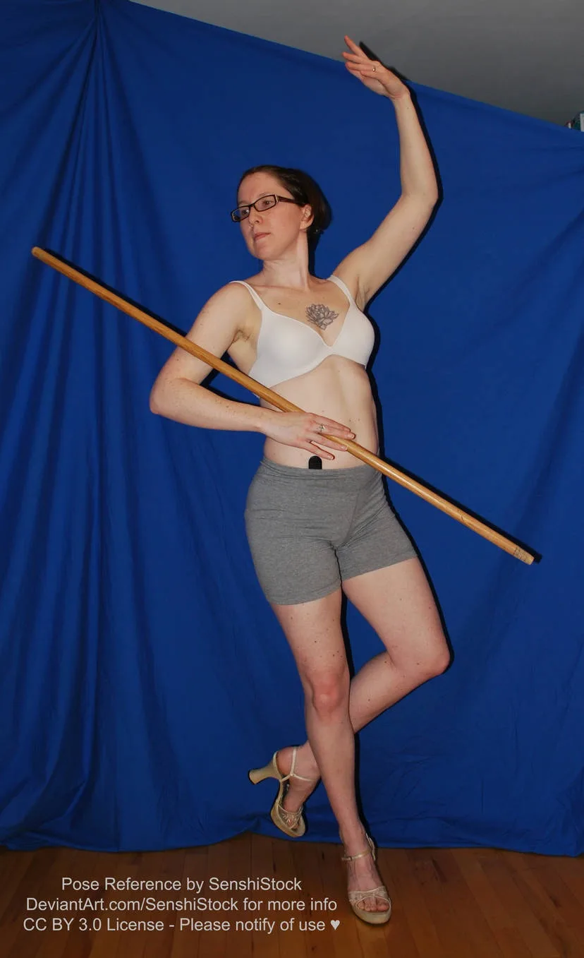 A woman in a white bra, gray shorts, and heels poses gracefully against a blue backdrop while holding a long wooden staff…