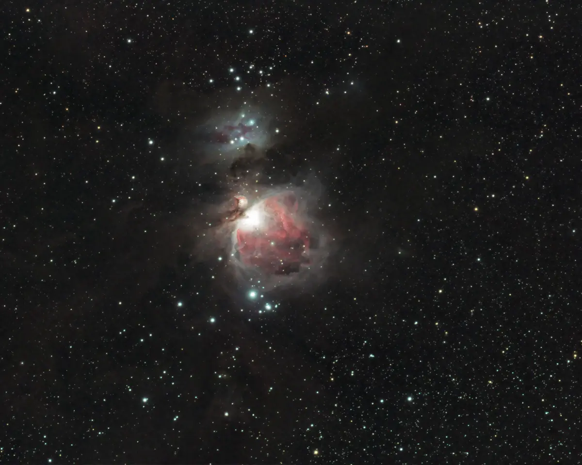 A deep-sky astrophotograph of the Orion Nebula, featuring a bright central star cluster surrounded by glowing red and blue…