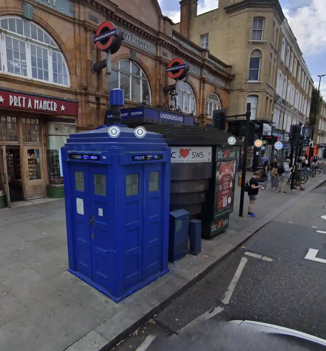 A blue police public call box, famously known as the TARDIS from Doctor Who, is situated on a sidewalk next to an…