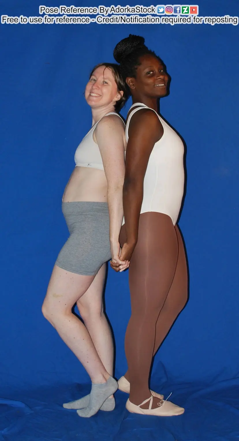 Two women stand back-to-back against a blue backdrop, holding hands, one wearing gray shorts and socks, the other in a…