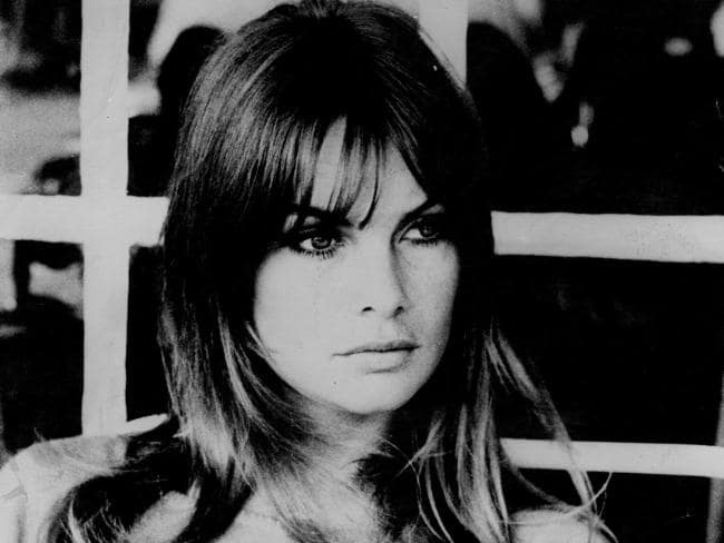 A black-and-white photo of a woman with long hair and bangs looking directly at the camera with a serious expression…