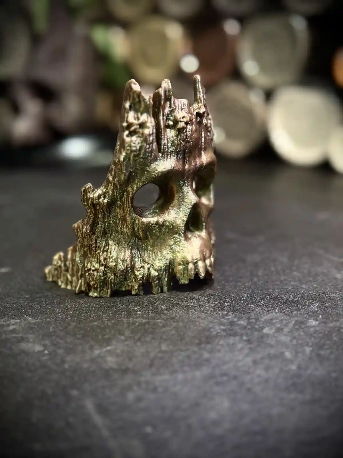 A close-up photo shows a small, textured, bronze-colored skull-shaped object with visible eye sockets and teeth, sitting on…