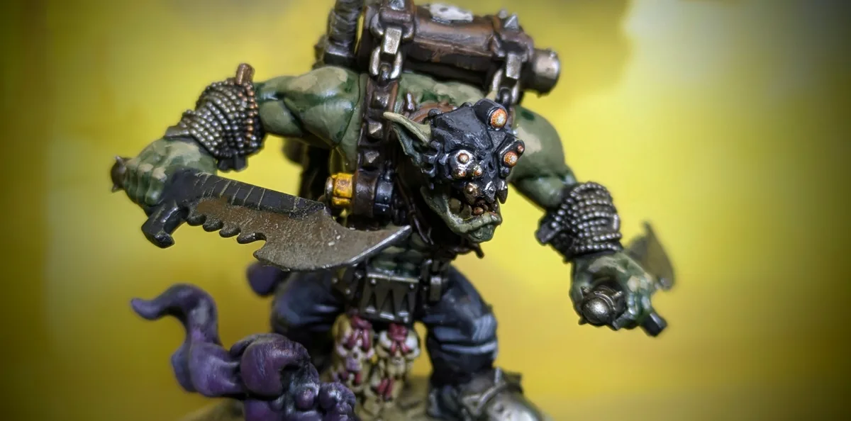 A close-up photo of a detailed, painted green-skinned fantasy miniature figure resembling a monstrous orc or goblin warrior…
