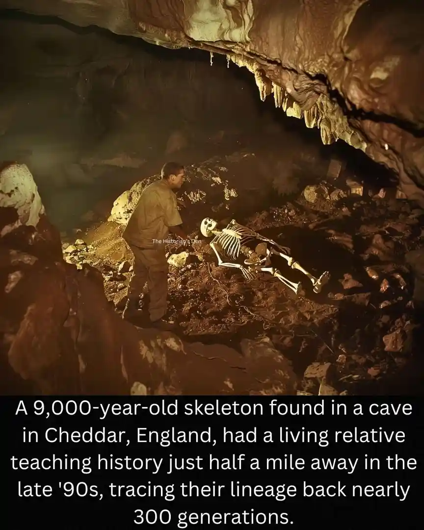 A man in work clothes stands in a dimly lit cave, looking at a human skeleton lying on rocky ground. The cave has…