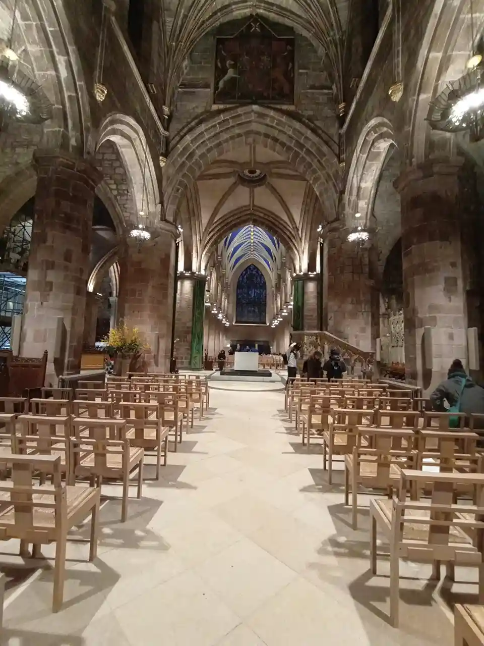The image shows the interior of a grand, empty Gothic cathedral with stone arches, wooden pews, and a distant altar. A few…