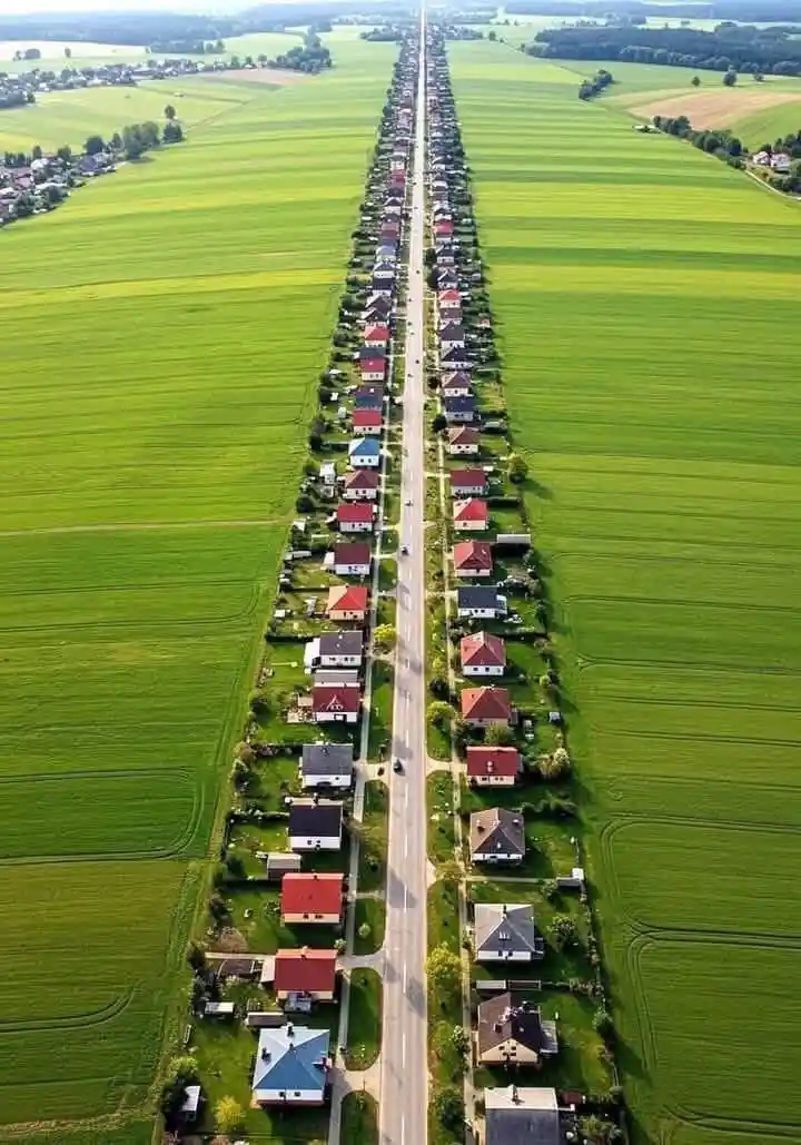an aerial view shows a long, straight road flanked by rows of houses on both sides, stretching into the distance between…