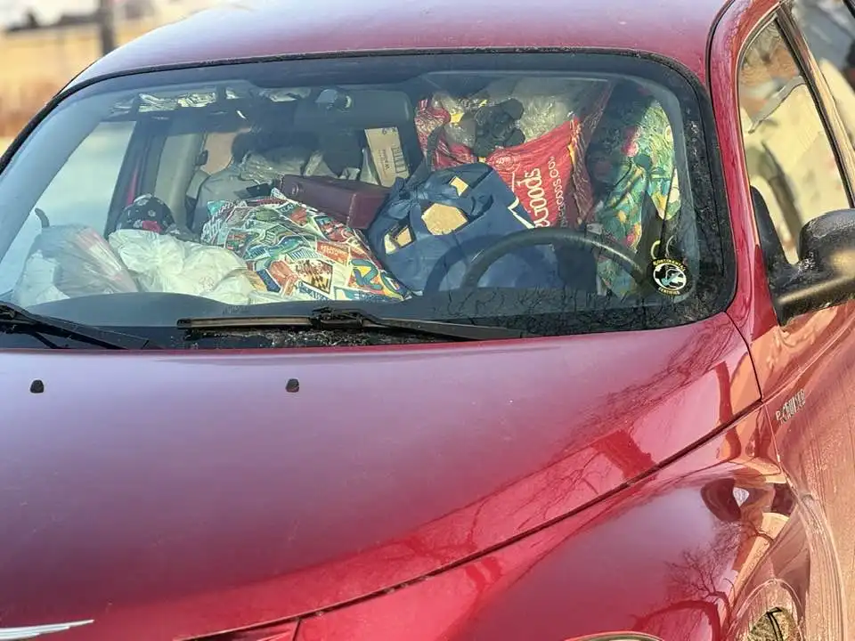 A red car's interior is visibly packed with clutter, including bags, a steering wheel, and various items, with a sticker on…