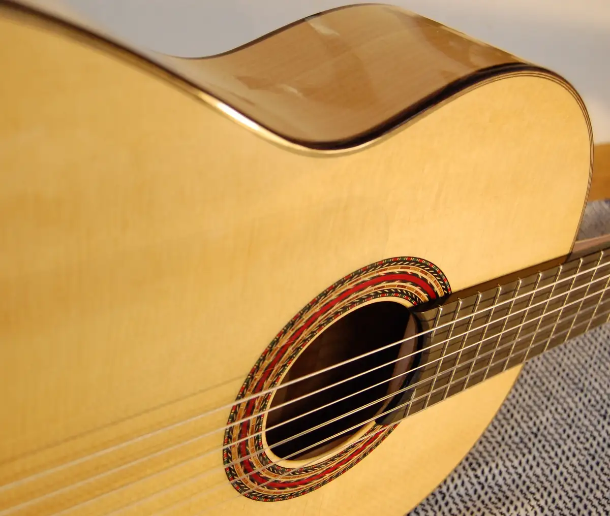 A close-up photo of a light-wood acoustic guitar's body, focusing on the soundhole with its decorative rosette and the…