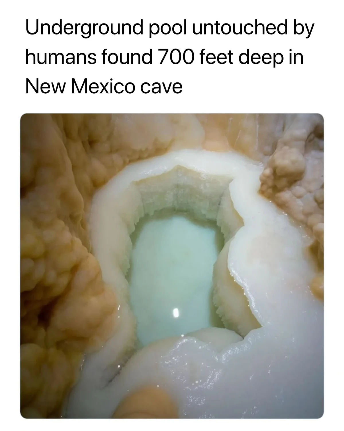 The image shows a close-up of a small, shallow pool of clear, light-blue water nestled within a cavernous, rocky formation…