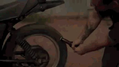 A man with tattoos on his arms is shown in a sequence of six frames, using a beer bottle to open the rear wheel of a…