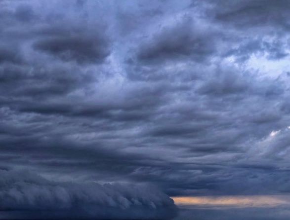 A dramatic, dark, and stormy sky with heavy, swirling clouds and a faint orange glow on the horizon. Overlaid text reads…