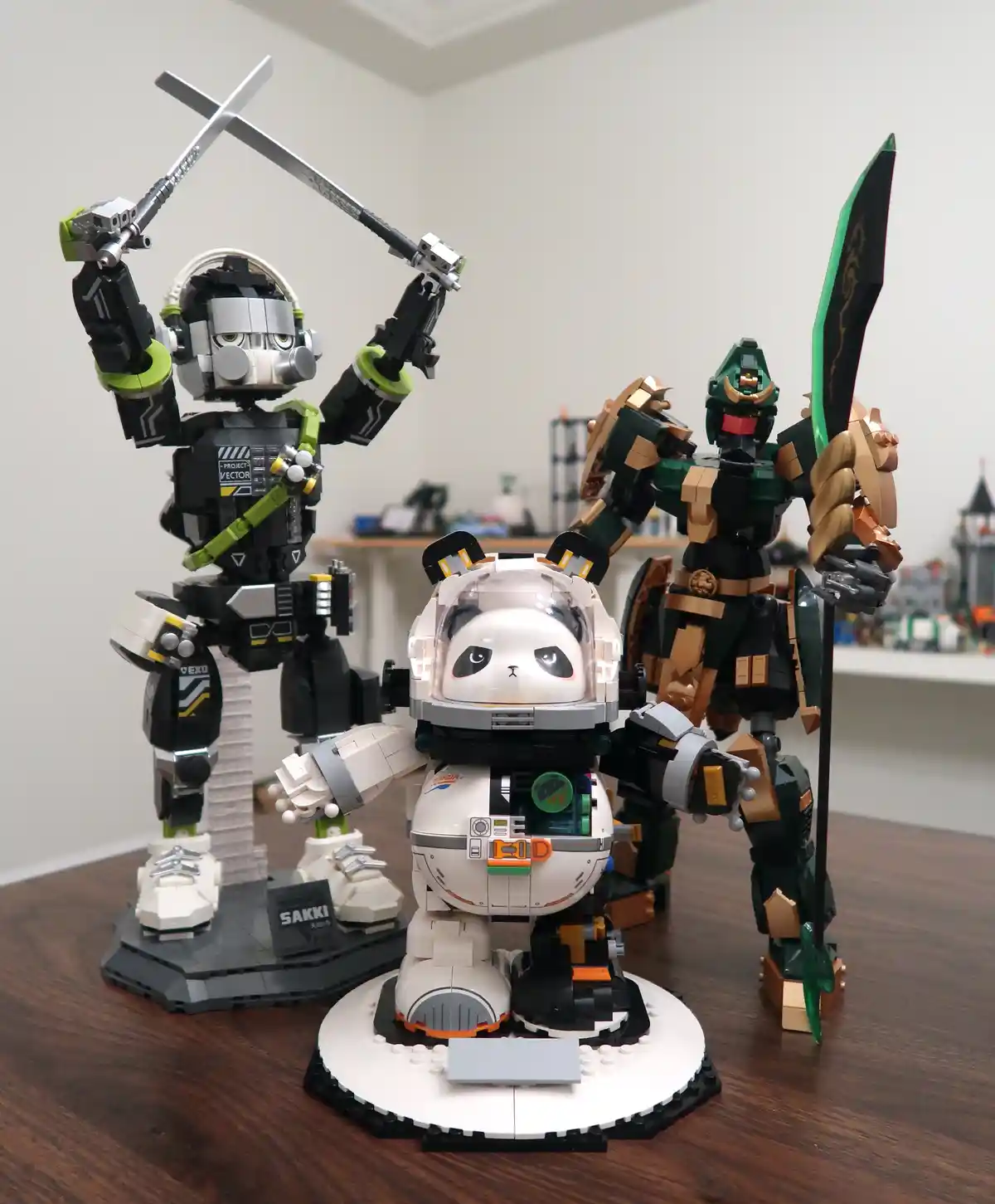 Three detailed robot models made of building blocks stand on a wooden table: a black and green robot with crossed swords, a…
