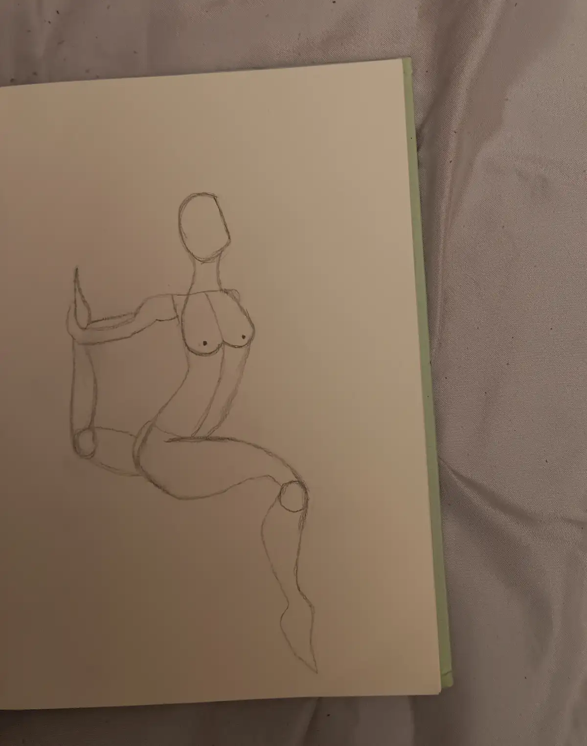 A simple pencil sketch on a notebook page shows a stylized, minimalist human figure with a round head, defined breasts, and…