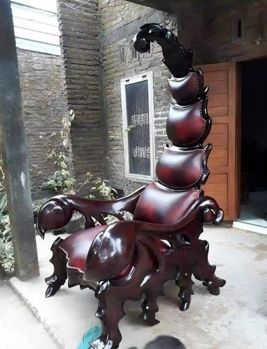 a highly polished, dark reddish-brown wooden chair shaped like a scorpion, with a curved tail rising vertically and pincers…