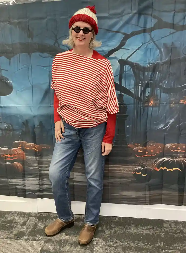 A person stands in front of a Halloween-themed backdrop featuring pumpkins and spooky trees, wearing a red-and-white striped…