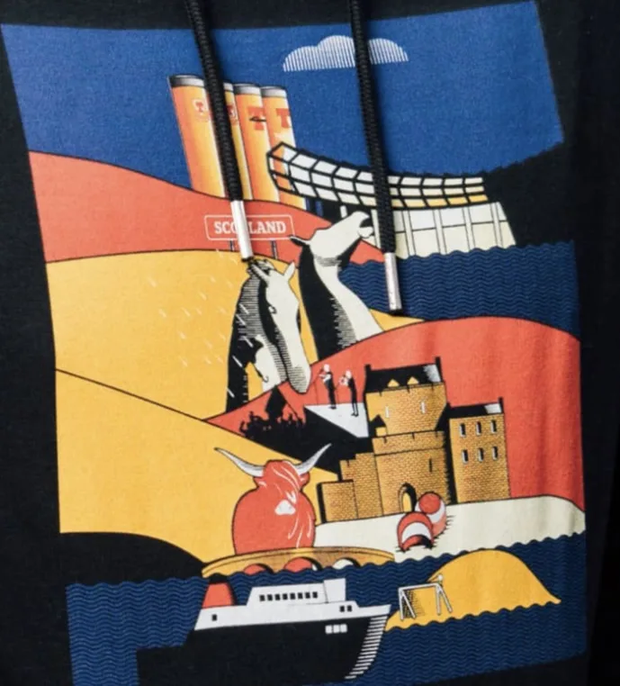 A close-up of a black hoodie with a colorful graphic print depicting iconic Scottish imagery including a red Highland cow, a…