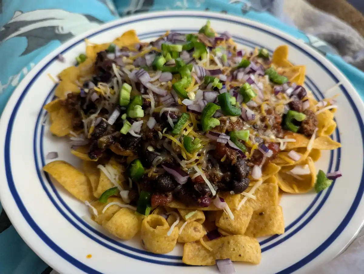 A close-up photo shows a white plate with blue concentric rings, filled with nachos. The nachos consist of tortilla chips…