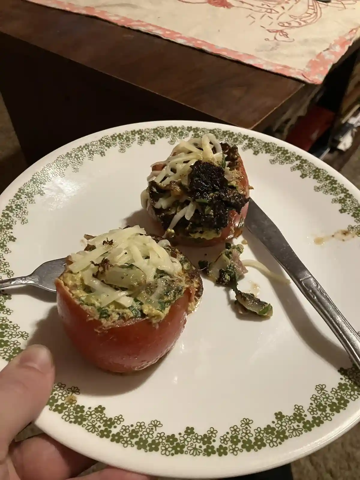 A close-up photo shows a plate with two baked stuffed tomatoes, one partially eaten with a fork and the other showing a…
