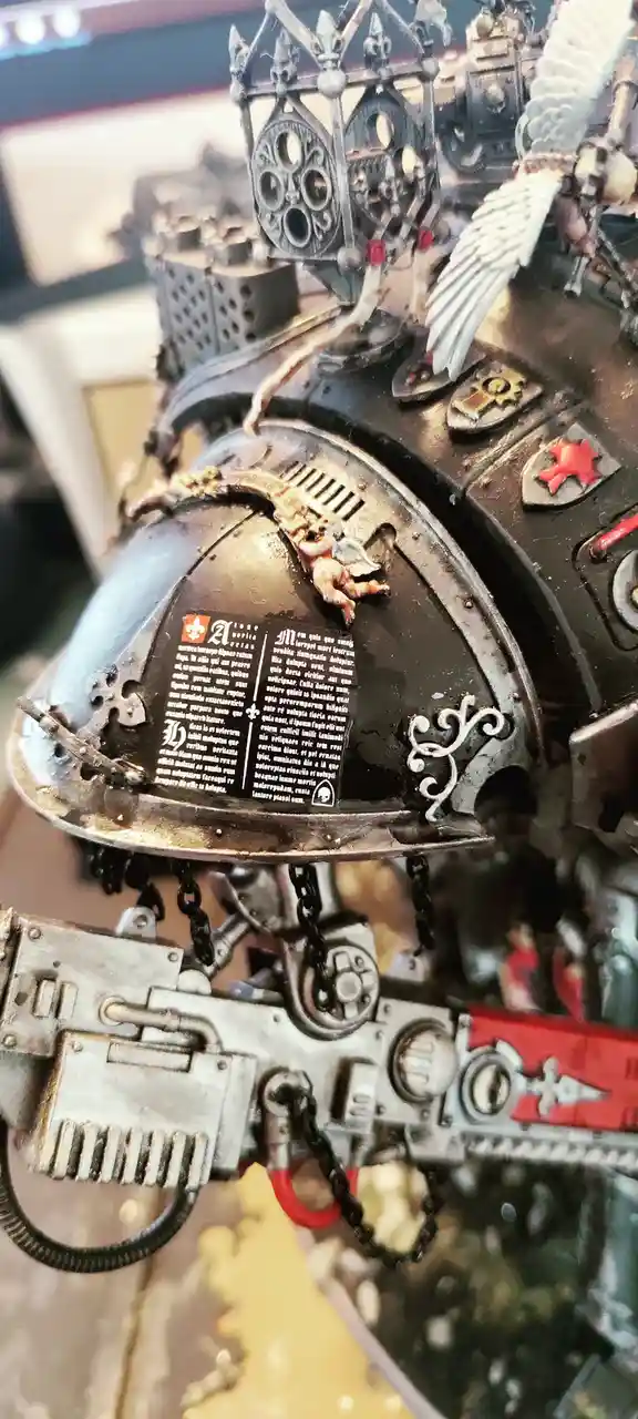 A close-up photo shows a highly detailed miniature of a heavily armored, gothic-style warrior, likely from Warhammer 40,000…