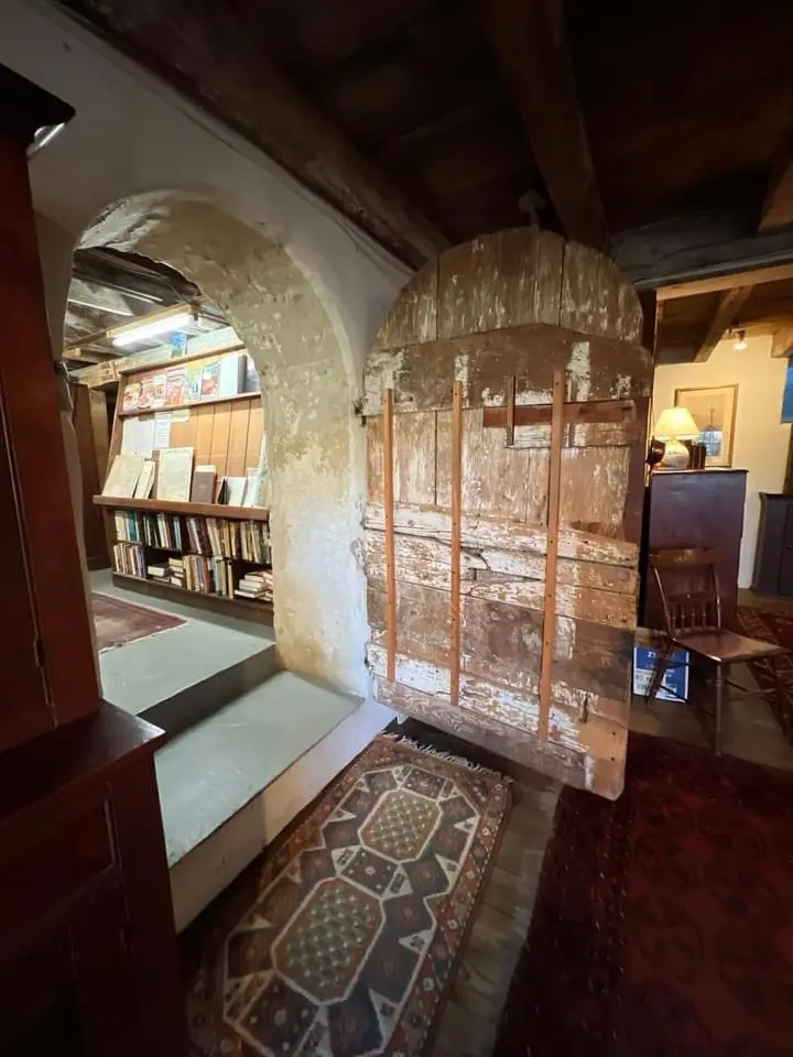 An old, weathered wooden door with peeling paint and visible wood grain stands in a rustic room with exposed beams and…