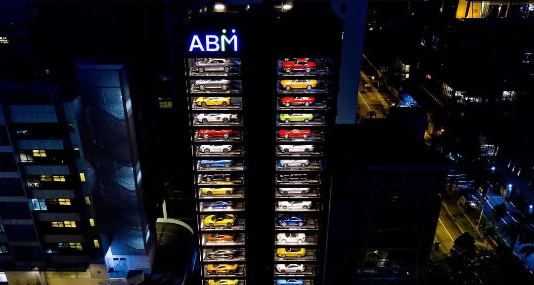 A nighttime aerial view of a tall building with a glowing 'ABM' sign at the top, featuring two vertical columns of brightly…