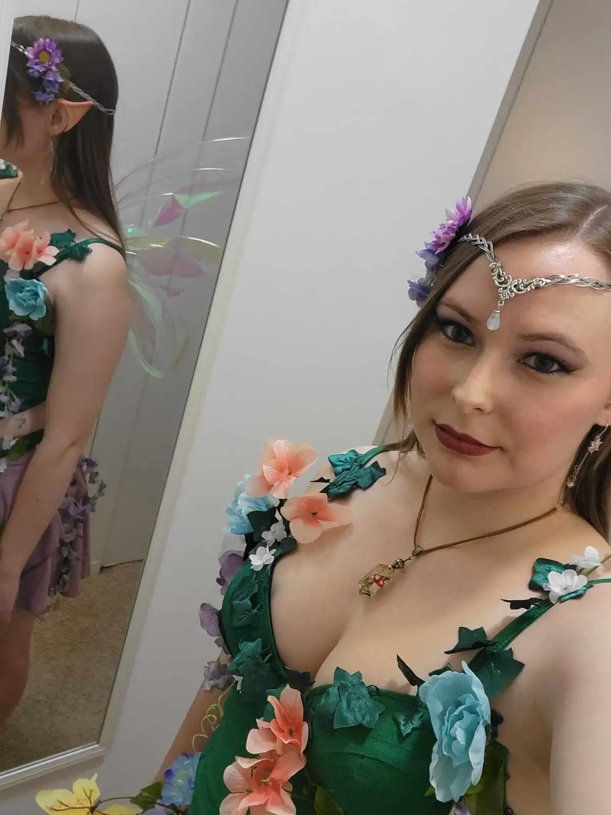 A woman in a detailed green fairy costume with floral embellishments, leafy straps, and a silver headpiece with purple…